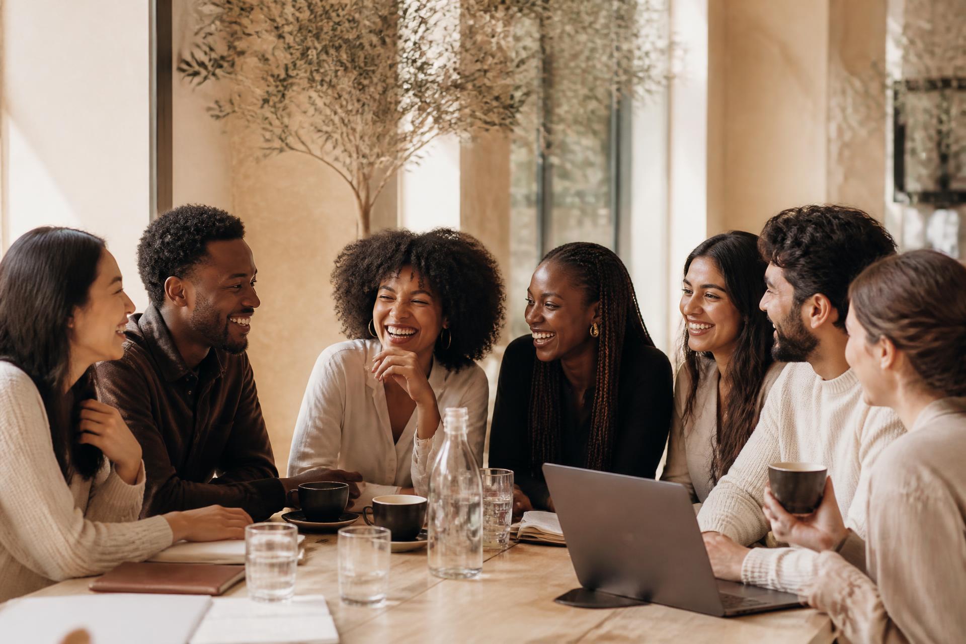 Four entrepreneurs laughing together around a marble table in a sunlit café